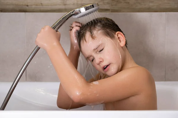 El niño sosteniendo la cabeza de la ducha y se lava la cabeza en el baño infancia saludable — Foto de Stock