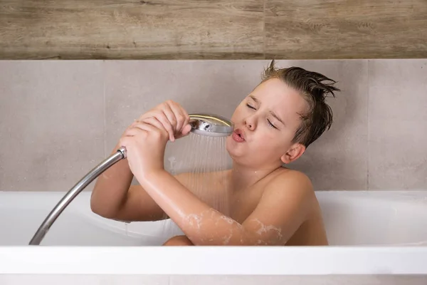 Niño feliz sosteniendo la cabeza de la ducha y cantando mientras se lava en baño infancia saludable — Foto de Stock