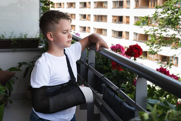 Triste enfant avec un bras cassé dans un plâtre regarde dans la cour du balcon — Photo