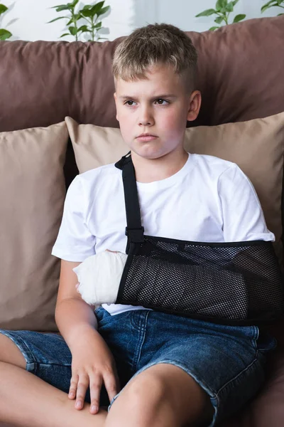 Triste menino com braço quebrado no elenco senta-se em casa na varanda. — Fotografia de Stock