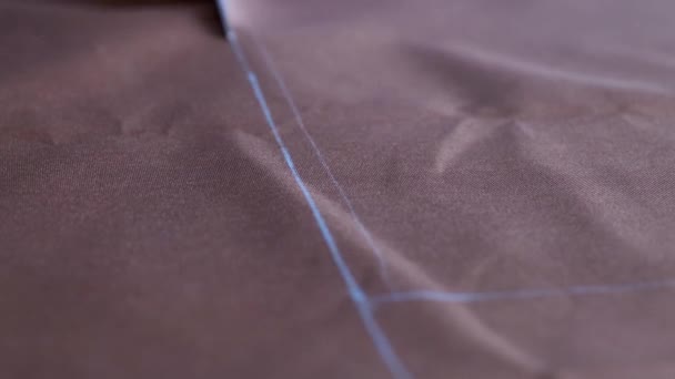 Manos de mujer con tijeras que cortan tela marrón según marcas en la mesa — Vídeos de Stock