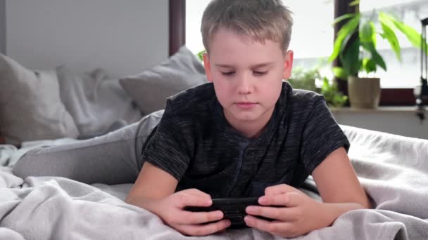 4K Boy gra w grę mobilną na smartfonie siedzi na łóżku w swoim pokoju — Wideo stockowe