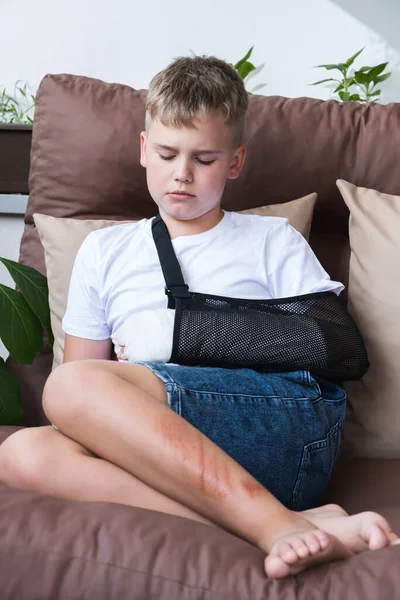 Criança triste com um braço partido no ambiente doméstico. Elenco na mão de menino. — Fotografia de Stock