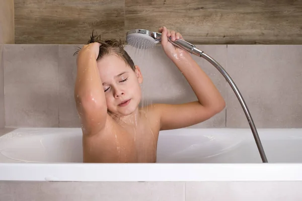 El niño sosteniendo la cabeza de la ducha y se lava la cabeza en el baño infancia saludable — Foto de Stock