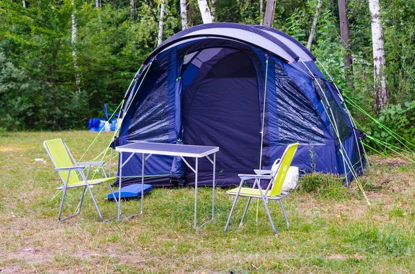 Installerat blått turisttält, campingbord och stolar i skogen på campingplatsen. — Stockfoto