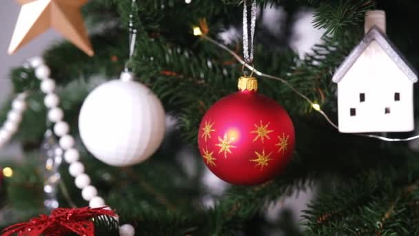 Різдвяні прикраси у вигляді кульок, будинку та дзвінка та вогнів на дереві — стокове відео