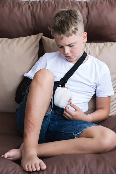 Rapaz triste com um braço partido e feridas na perna senta-se em casa na varanda. — Fotografia de Stock