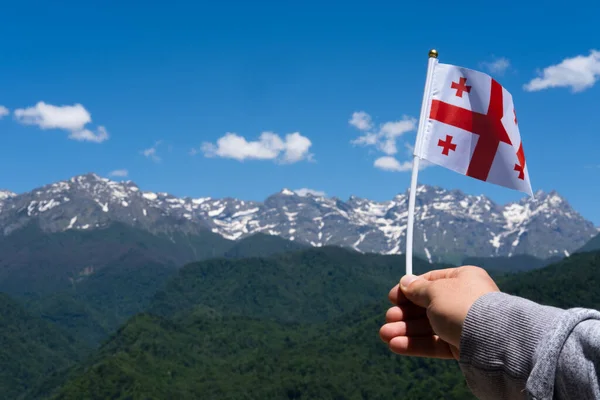 Georgian flag in mans hand on Background of Mountains and Blue Sky. Georgian national flag