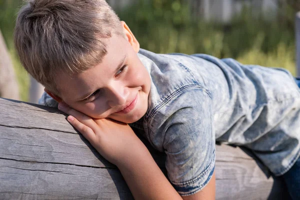 Yakışıklı sarışın çocuk parktaki tahta kirişin üzerinde yatıyor.. — Stok fotoğraf