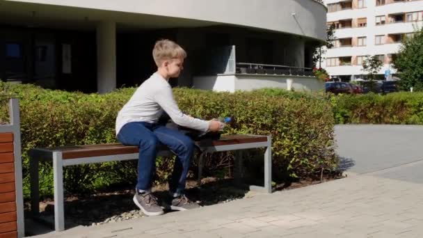 Ragazzo biondo prende una bottiglia d'acqua dallo zaino della scuola e beve con sete — Video Stock