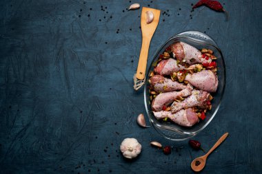 Çiğ tavuk bacağı ve arka planda şeffaf bir tabakta bolca baharat..