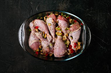 Çiğ tavuk bacağı ve siyah arka planda şeffaf bir tabakta bolca baharat..