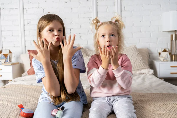 Duas meninas estão sentadas na cama no quarto e mostrando sua nova manicure. — Fotografia de Stock