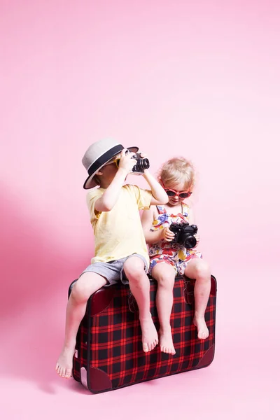 Viajes: Niños un niño y una niña juegan en los turistas, se sientan en una gran maleta roja y toman fotos. —  Fotos de Stock