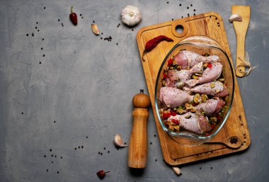 Çiğ tavuk bacağı ve bir sürü baharat. Gri arka planda şeffaf bir tabakta..