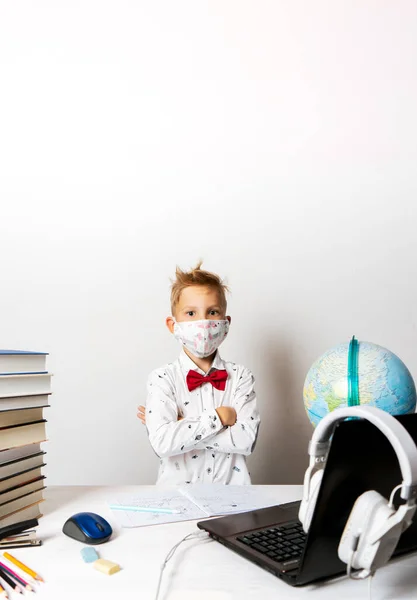 Um menino em quarentena usando uma máscara com um laptop está passando por treinamento escolar remotamente. — Fotografia de Stock