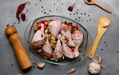 Çiğ tavuk bacağı ve bir sürü baharat. Gri arka planda şeffaf bir tabakta..