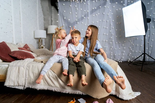 Tiga anak di kamar tidur di tempat tidur tertawa dan bermain-main. — Stok Foto