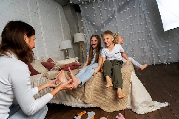 Anya a hálószobában az ágyon szórakozás csiklandozza a gyerekek, fiúk és lányok lábát. — Stock Fotó