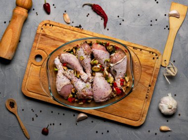 Çiğ tavuk bacağı ve bir sürü baharat. Gri arka planda şeffaf bir tabakta..