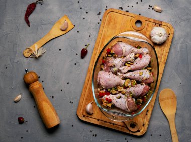 Çiğ tavuk bacağı ve bir sürü baharat. Gri arka planda şeffaf bir tabakta..