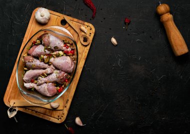 Çiğ tavuk bacağı ve siyah arka planda şeffaf bir tabakta bolca baharat..