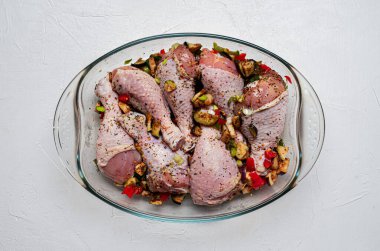 Çiğ tavuk bacağı ve beyaz arka planda şeffaf bir tabakta bolca baharat..