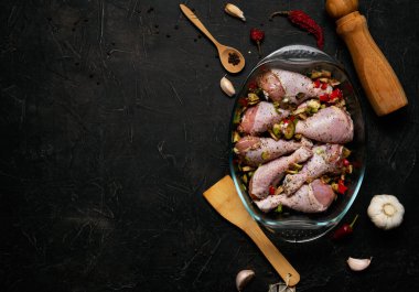 Çiğ tavuk bacağı ve siyah arka planda şeffaf bir tabakta bolca baharat..