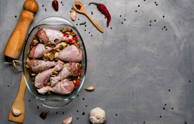 Çiğ tavuk bacağı ve bir sürü baharat. Gri arka planda şeffaf bir tabakta..