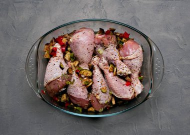 Çiğ tavuk bacağı ve bir sürü baharat. Gri arka planda şeffaf bir tabakta..