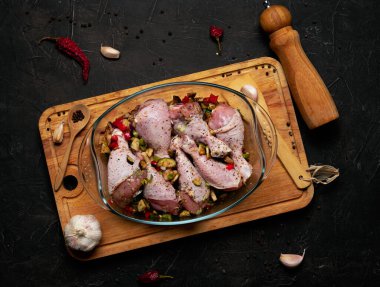 Çiğ tavuk bacağı ve siyah arka planda şeffaf bir tabakta bolca baharat..