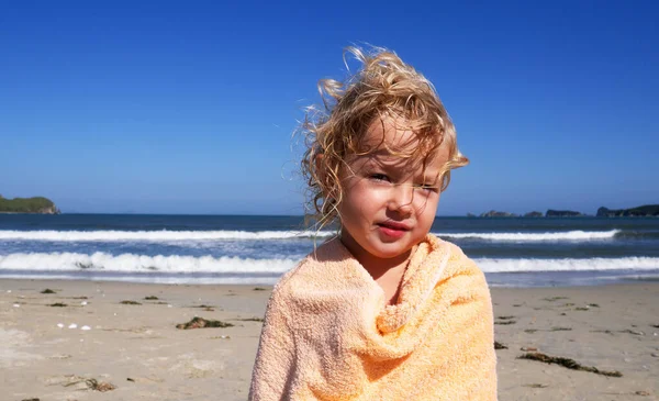 Medio primer plano lindo niño con pelo rubio rizado sensación de frío en el calentamiento de la playa envuelto en toalla — Foto de Stock
