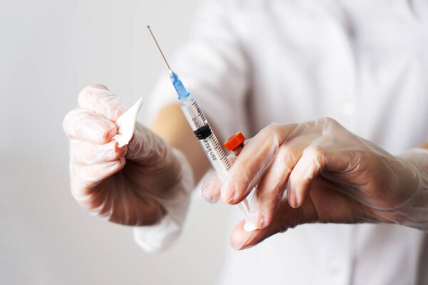 Closeup female doctor hands in gloves syringe with needle full of drug and disinfection cotton swab