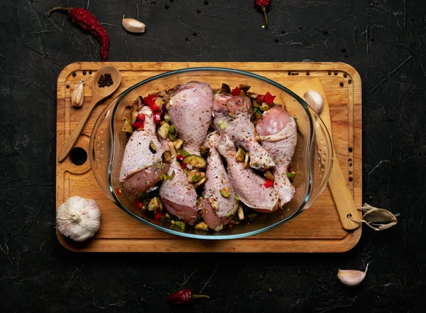 Çiğ tavuk bacağı ve siyah arka planda şeffaf bir tabakta bolca baharat..