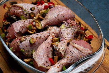 Çiğ tavuk bacağı ve arka planda şeffaf bir tabakta bolca baharat..