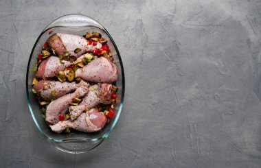 Çiğ tavuk bacağı ve bir sürü baharat. Gri arka planda şeffaf bir tabakta..