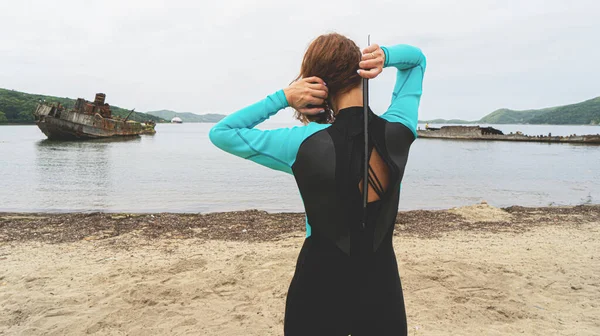少女は海岸に立って、曇りの日に青いウェットスーツを着る. — ストック写真