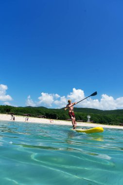 Adam güneşli bir günde sarı bir SUP tahtasının üzerinde kürek çekiyor..
