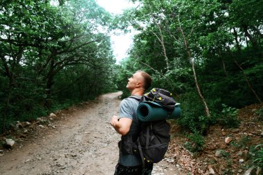Büyük bir sırt çantalı bir yürüyüşçü sık bir ormanda yol boyunca yürür..