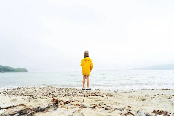 黄色いウインドブレーカーの小さな男の子が一人で海の砂浜に立っている. — ストック写真