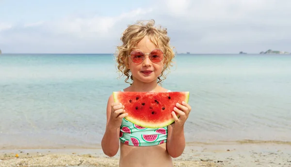 Retrato niña lamiendo rodaja de sandía fresca posando en la playa teniendo diversión y emoción positiva — Foto de Stock