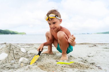 Deniz kabuklarıyla kumdan kule inşa eden sevimli çocuk yaz mevsiminde tropikal tatil köyünde kürek kemiği kullanıyor.