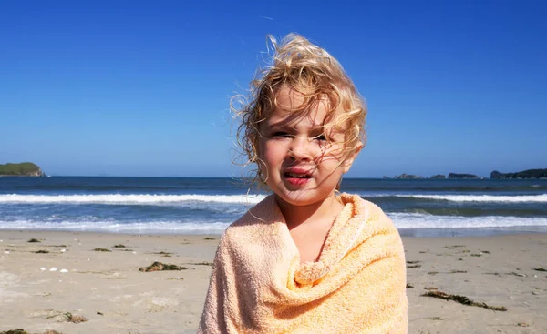 Medio primer plano lindo niño con pelo rubio rizado sensación de frío en el calentamiento de la playa envuelto en toalla — Foto de Stock