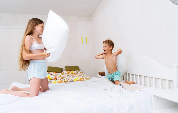 Funny brother and sister fighting pillow on bed morning bedroom kids boy and girl playing together — Stock Photo, Image