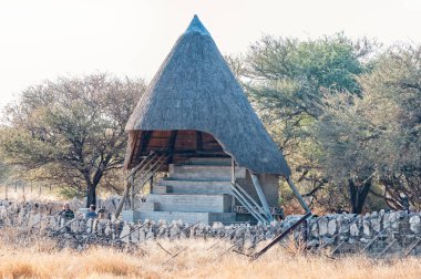 ETOSHA ULUSAL PARK, NAMIBIA - 12 Haziran 2012: Okaukeujo Dinlenme Kampı 'ndaki su birikintisi bakış açısında bir pavyon. Turistler görünür.