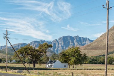 FRANSCHHOEK, Güney Afrika - 12 Nisan 2021: Batı Cape Eyaleti Franschhoek yakınlarında bir çiftlik evi. Hottentots-Holland Dağları ve güç altyapısı görülebilir.