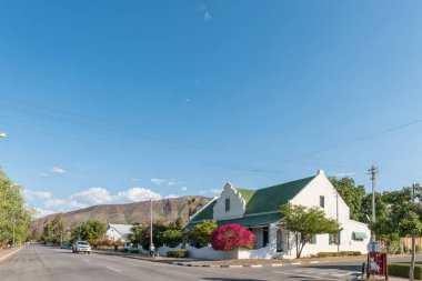 PRINCE ALBERT, GÜNEY AFRİKA - 20 Nisan 2021: Batı Cape Eyaleti 'ndeki Prens Albert' ta tarihi bir evi olan bir sokak sahnesi. Köpeği gezdiren bir araç ve bir insan görülebilir.