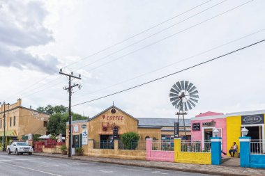 WILLOWMORE, GÜNEY AFRİKA - 21 Nisan 2021: Doğu Cape Eyaleti 'ndeki Willowmore' da iş yerleri ve araçlarla dolu bir sokak sahnesi. Bir yel değirmeni görünür.