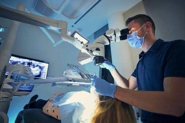 现代牙科手术中的牙科医生通过显微镜检查年轻患者的牙齿 — 图库照片
