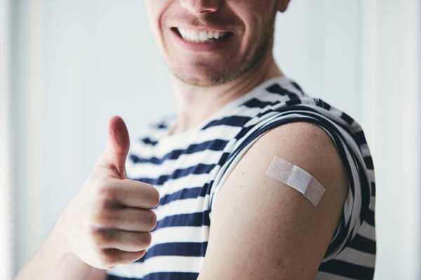 Happy young man showing thumb up and his arm after vaccination. Themes prevention, vaccine and health care during pandemic covid-19.